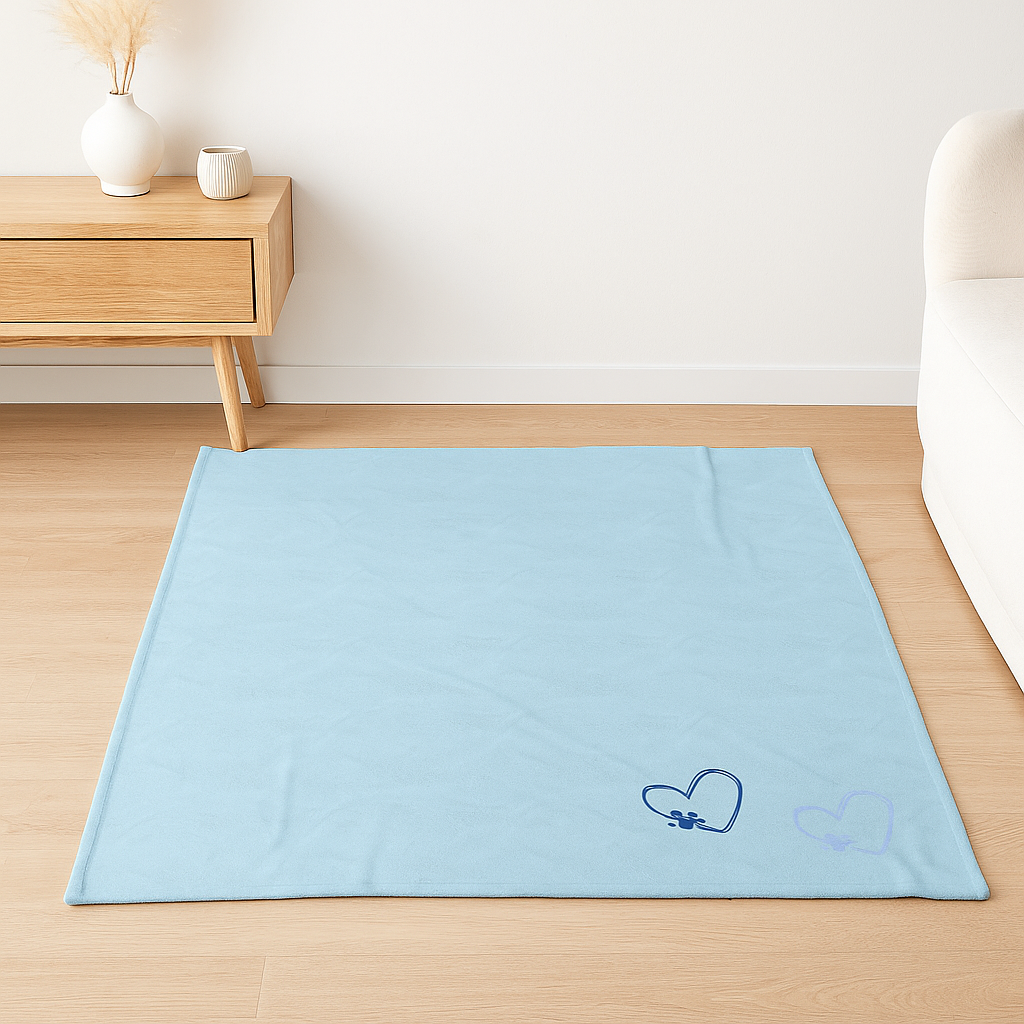 A soft light blue velveteen blanket with dark blue and pale paw heart graphics, styled in a cozy, light-toned room.