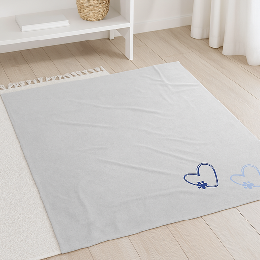 A light gray velveteen blanket with blue heart and paw print designs, laid out on light wooden flooring.