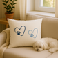 White pillow with blue paw print hearts on a beige couch, next to a sleeping Maltese dog – cozy home interior